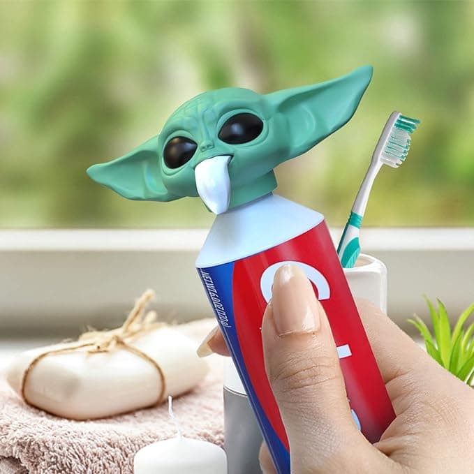 Cute Baby Y-oda toothpaste cap squeezing paste from his mouth, perched on a tube, making brushing teeth weirdly delightful for kids and Star Wars fans.