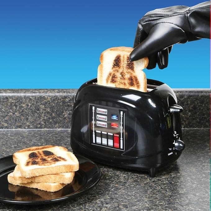 Darth Vader-themed toaster with two slices of bread marked with the Empire logo, sitting on a kitchen counter ready to toast with galactic menace.