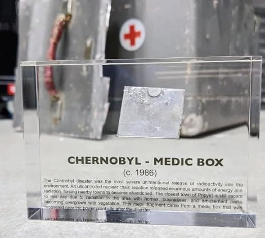 A small acrylic-encased fragment labeled as a Chernobyl medic box relic, displayed as a historical nuclear artifact.