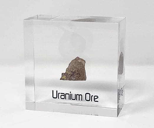 A novelty paperweight containing a chunk of uranium ore, sealed in a clear container and labeled for display or scientific curiosity.